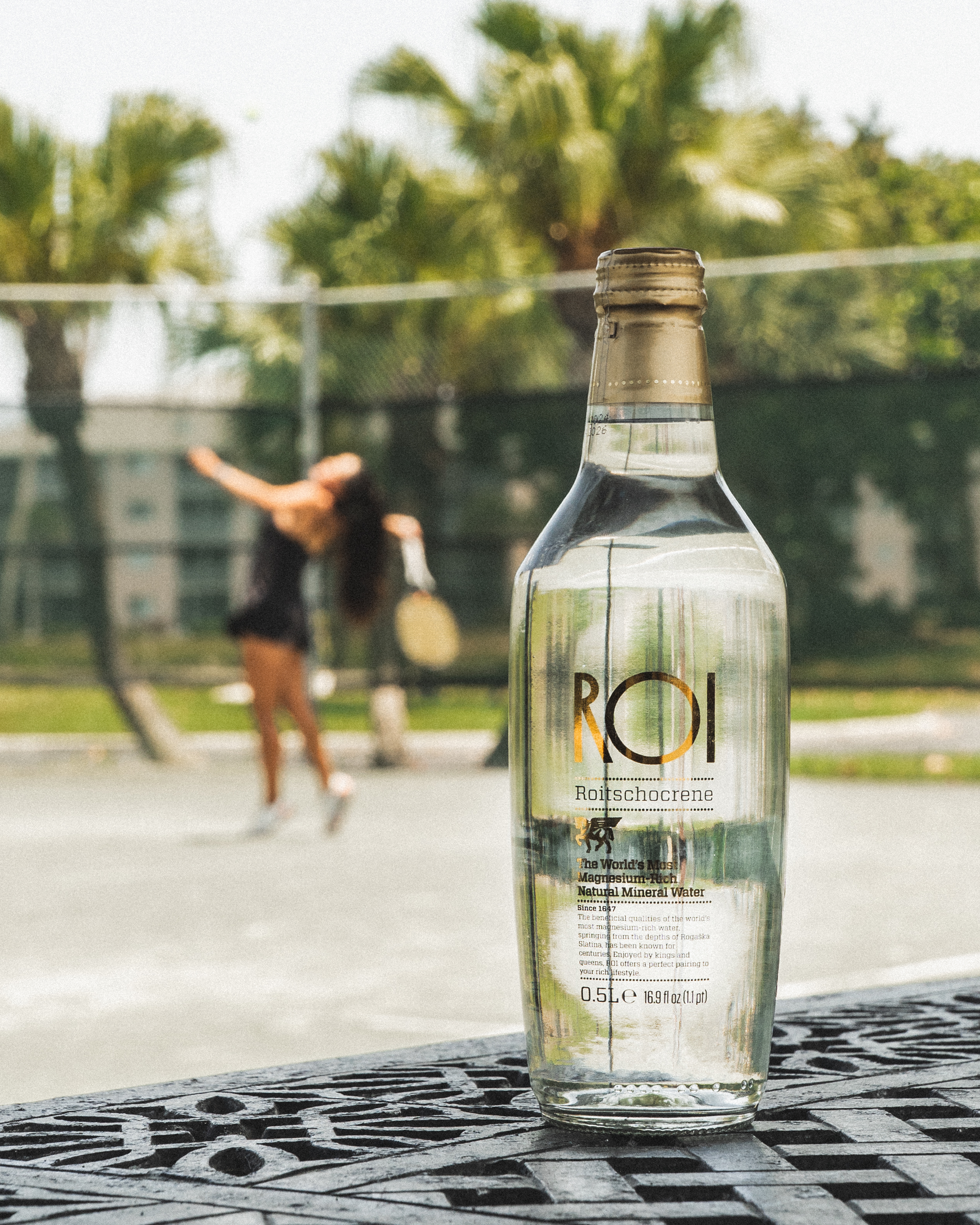 A bottle of mineral water on a table with a tennis player in the background.