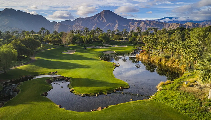 Scenic golf course with mountains, trees, and a pond under a cloudy sky.