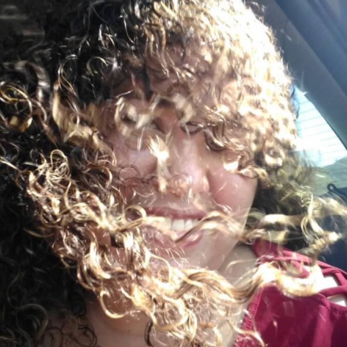 Person with curly hair smiling, hair covering face.