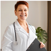 Person in a white coat with a stethoscope, holding a clipboard, smiling.
