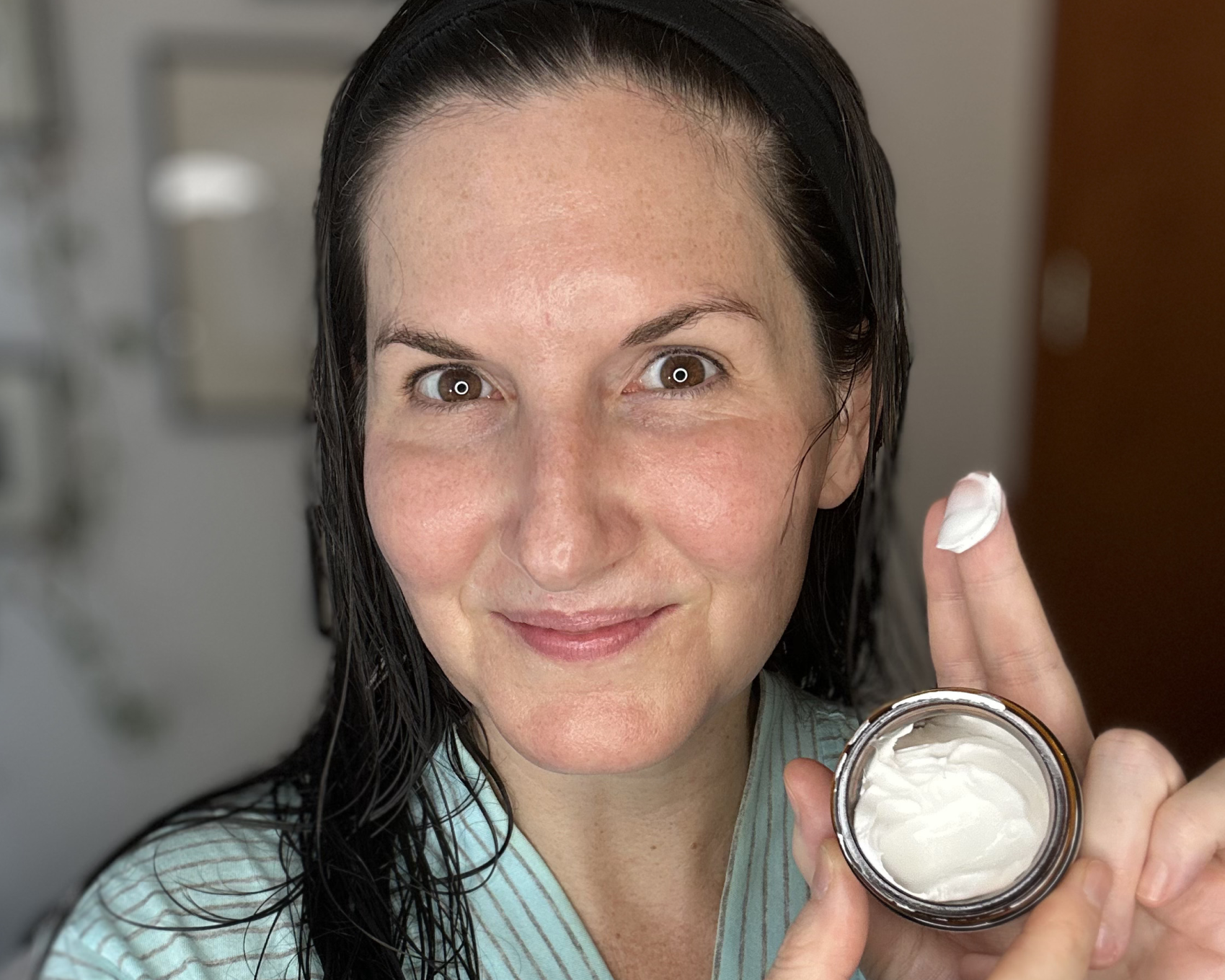 Person holding facial cream jar, applying cream with finger.