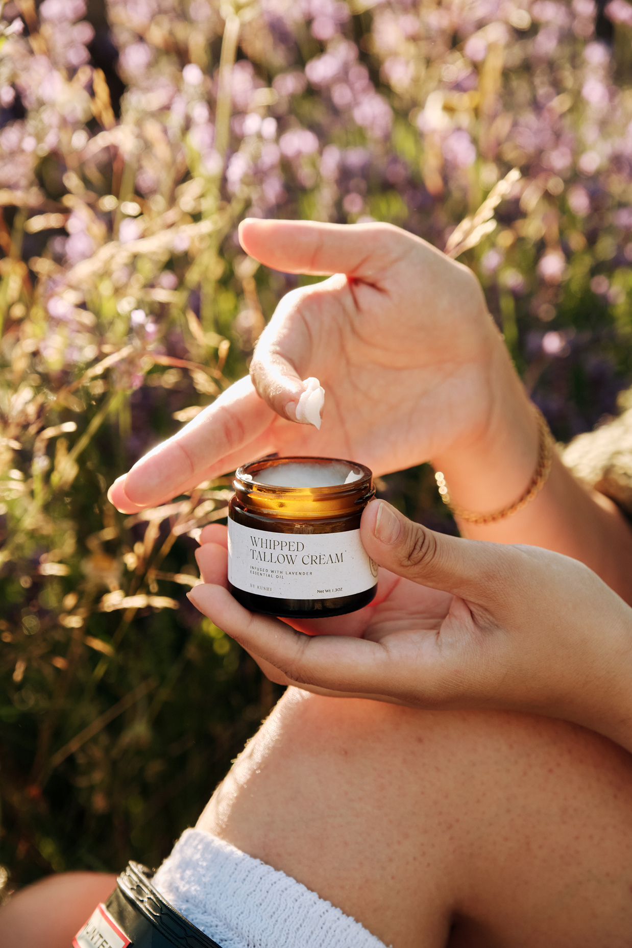 Hands holding a jar of whipped tallow cream outdoors.
