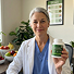 A woman in a white lab coat smiles while holding up a white bottle with a green label.