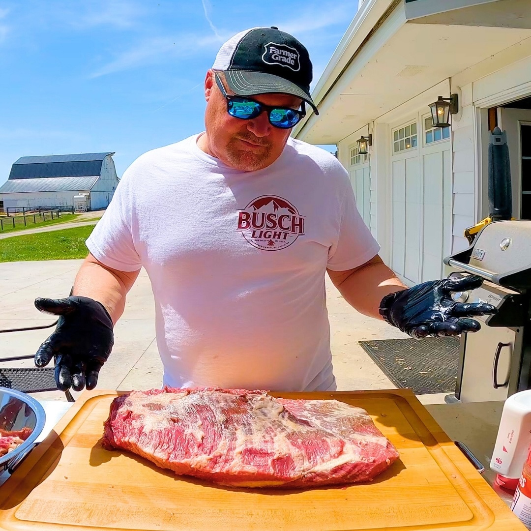 Person preparing raw meat on a wooden board outdoors.