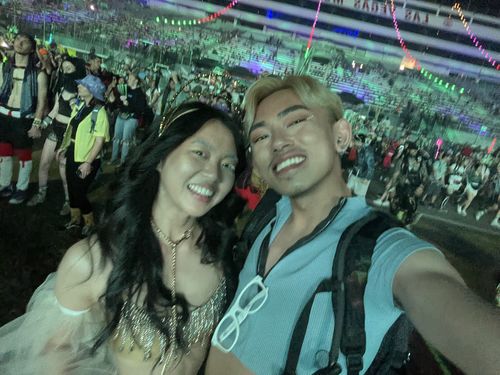 A man and a woman smiling for a selfie in a large crowd at a nighttime festival.