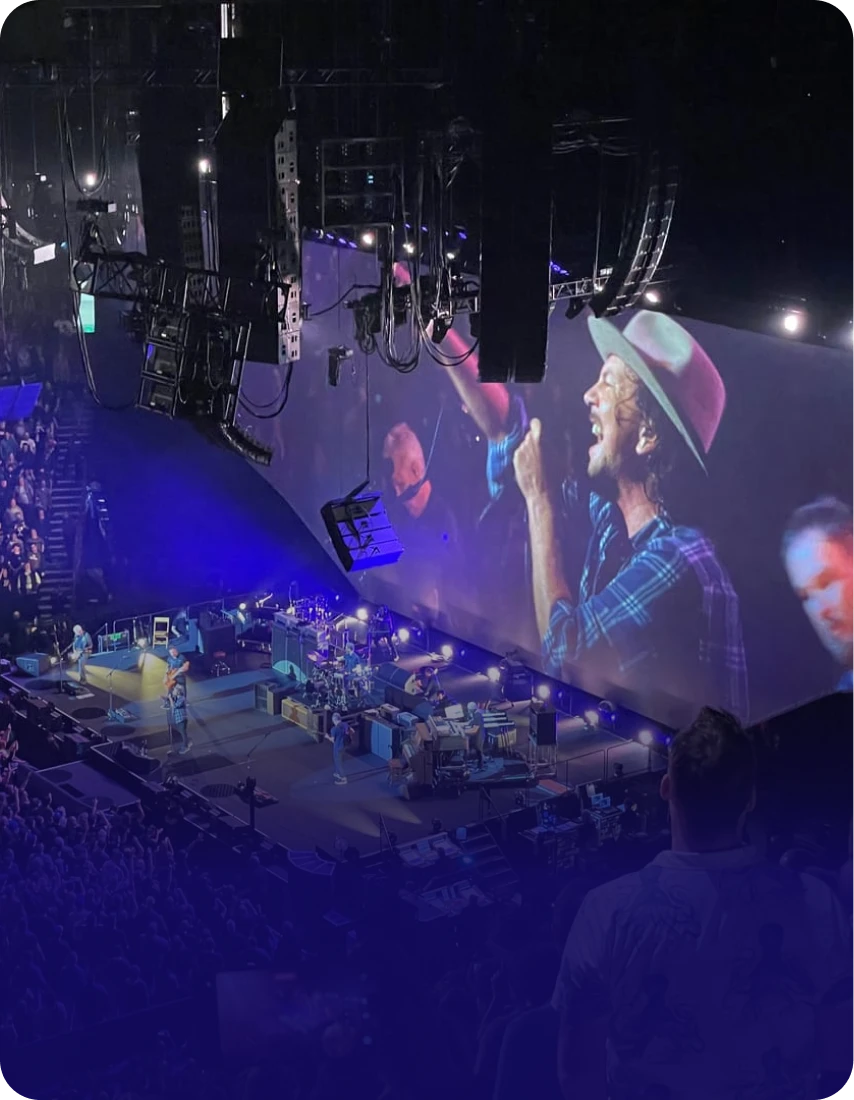 A high-angle view of a band performing on a concert stage with a large screen showing the singer.
