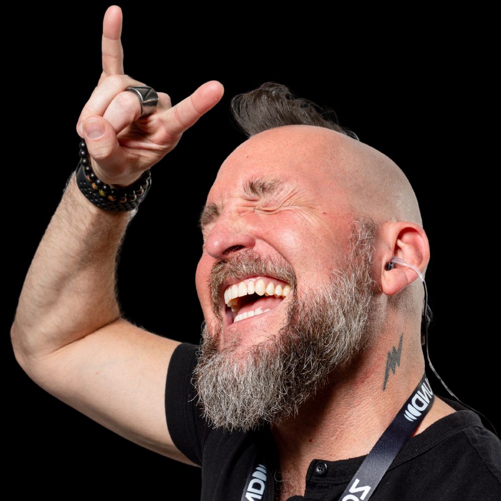 Man with beard making rock hand gesture, smiling.