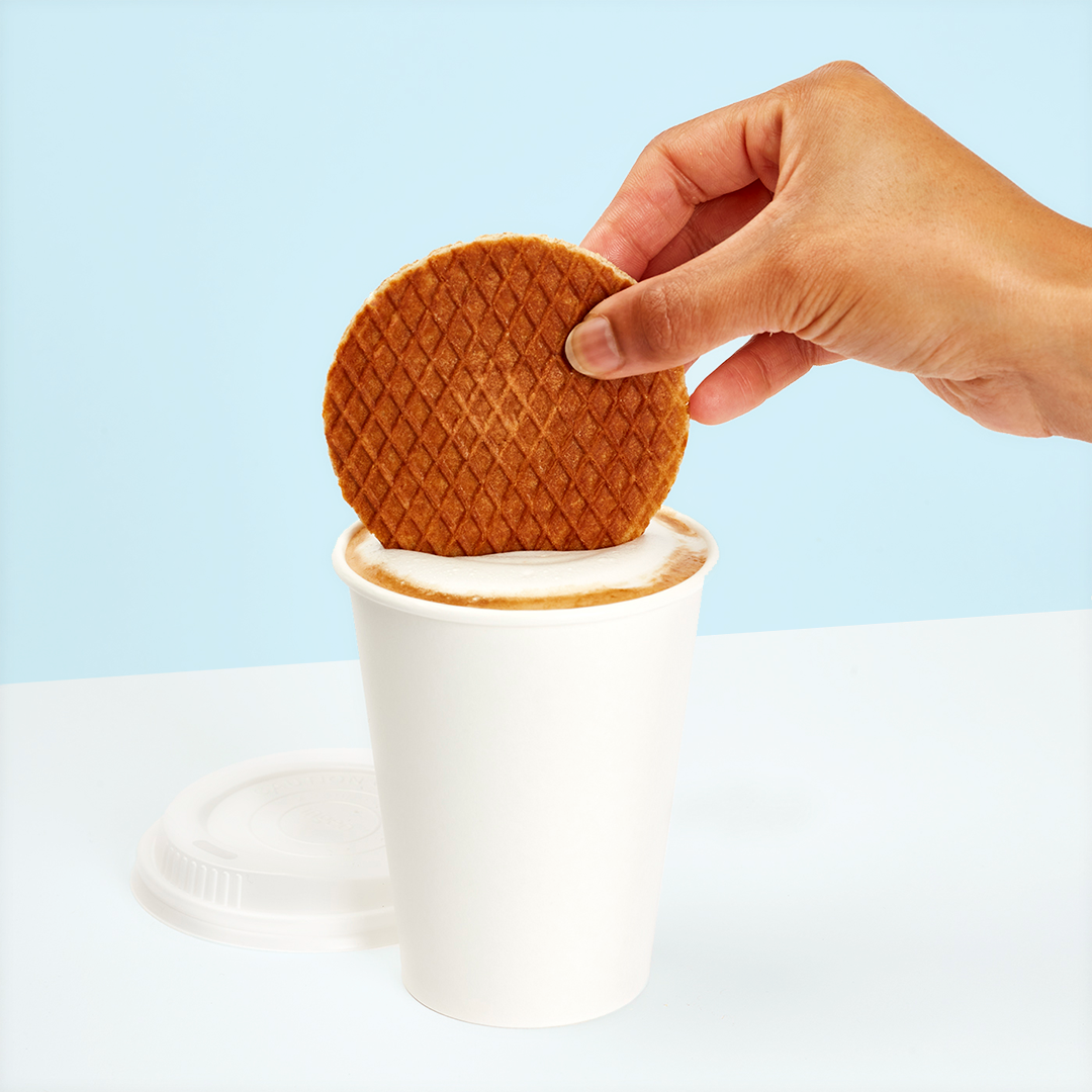 Hand placing a waffle cookie on a cup of coffee.
