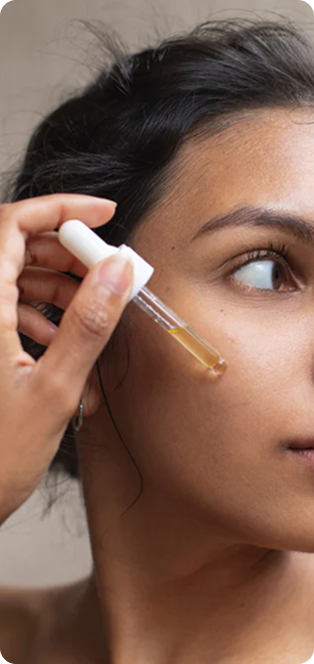 A close-up of a person applying a yellow serum to their cheek with a glass dropper.
