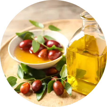 Bottle of oil and bowl with red berries and leaves on a wooden surface.