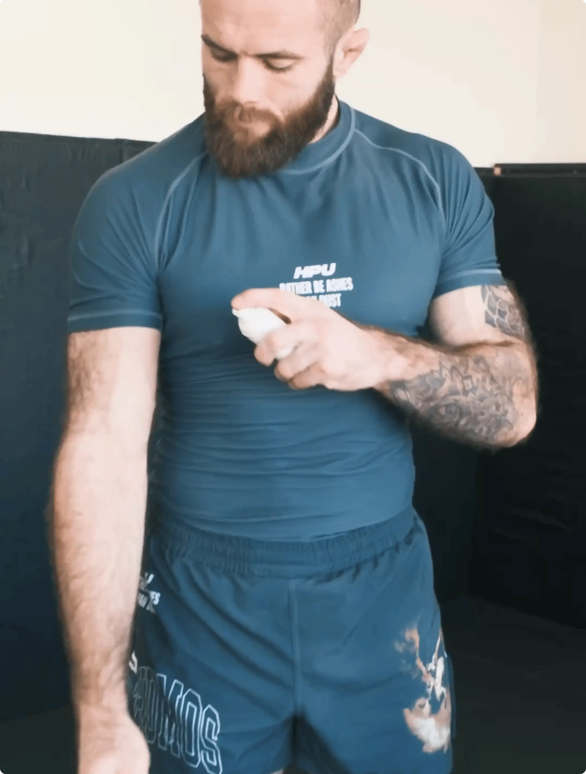 Man applying liquid to arm wearing athletic gear in a gym setting.