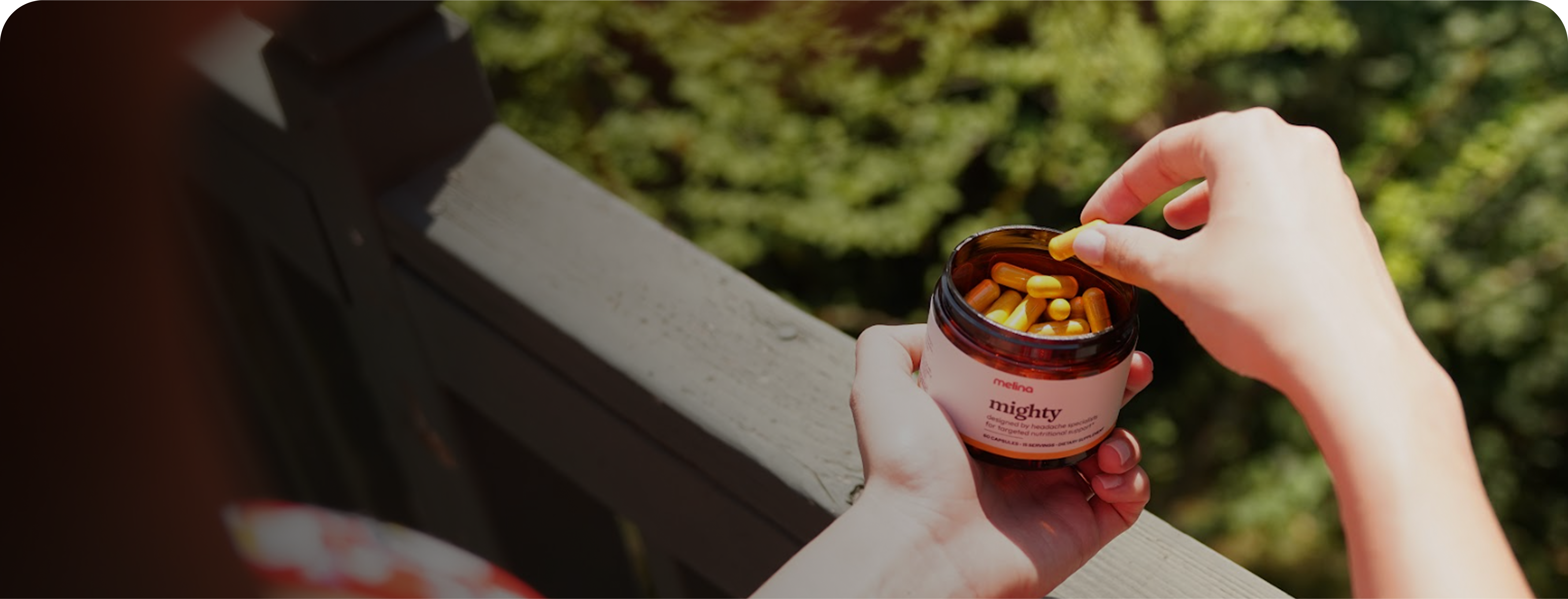 Hand holding a jar of orange capsules outdoors.