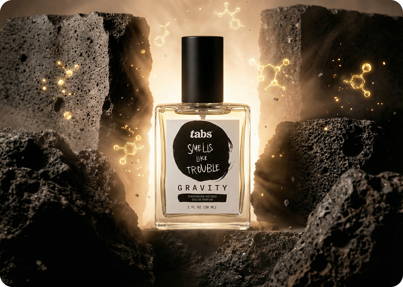 A bottle of Tabs Gravity perfume sits between dark rocks with glowing molecules floating around it.