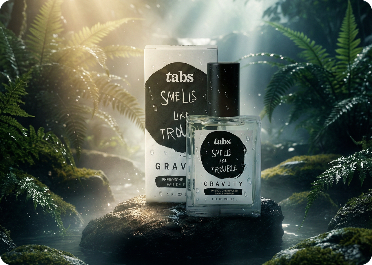 A bottle and box of 'tabs Smells Like Trouble' perfume on a wet rock in a misty jungle.