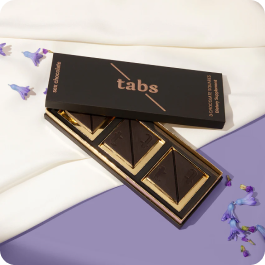 Box of chocolate tabs with flowers on fabric and purple surface.