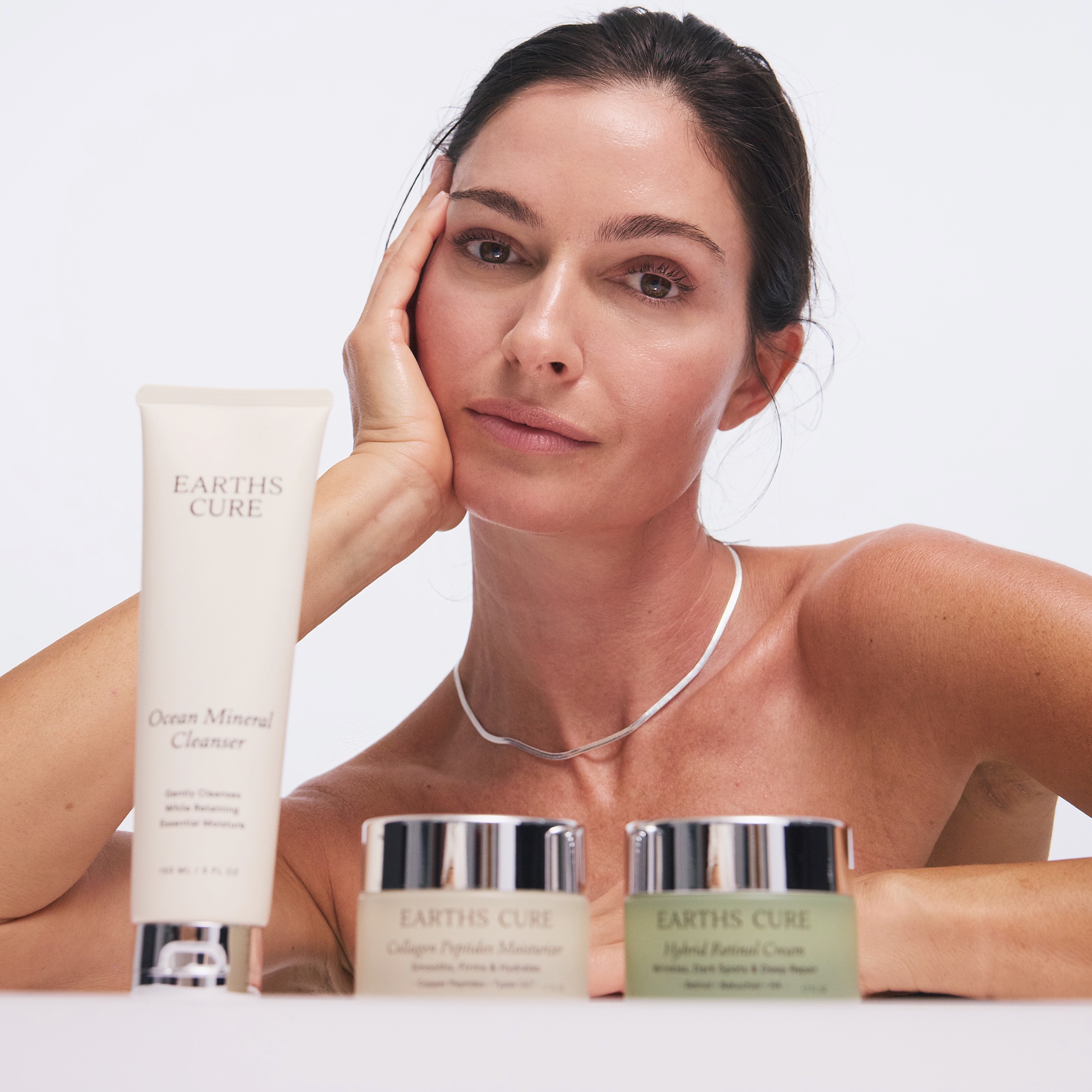 Woman posing with Earth's Cure skincare products on a white background.