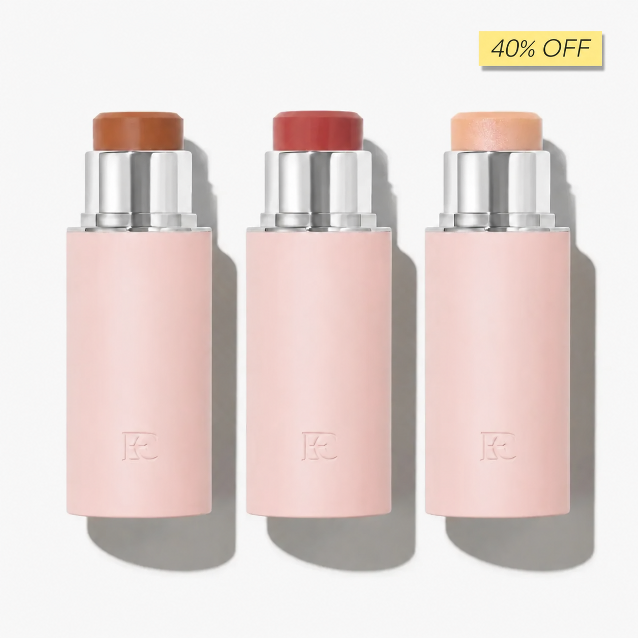 Three makeup sticks in pink tubes, showing shades of brown, red, and peach, on a white background.