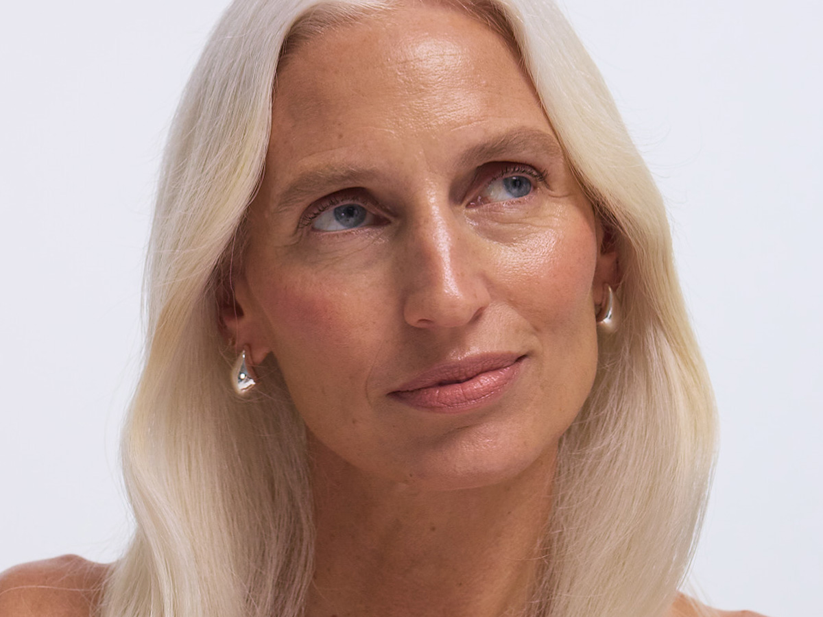 A person with long blonde hair and silver earrings looking upwards.