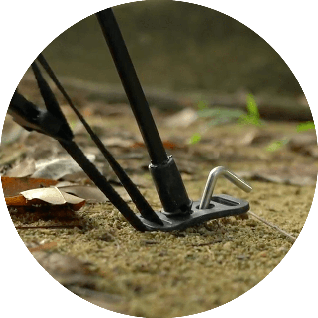Close-up of a tent stake securing a pole on sandy ground.