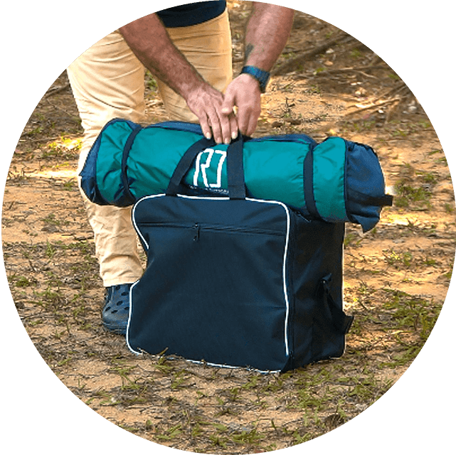 Person packing a rolled-up tent into a black bag outdoors.