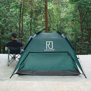 Person sitting near a green tent in a forest setting.