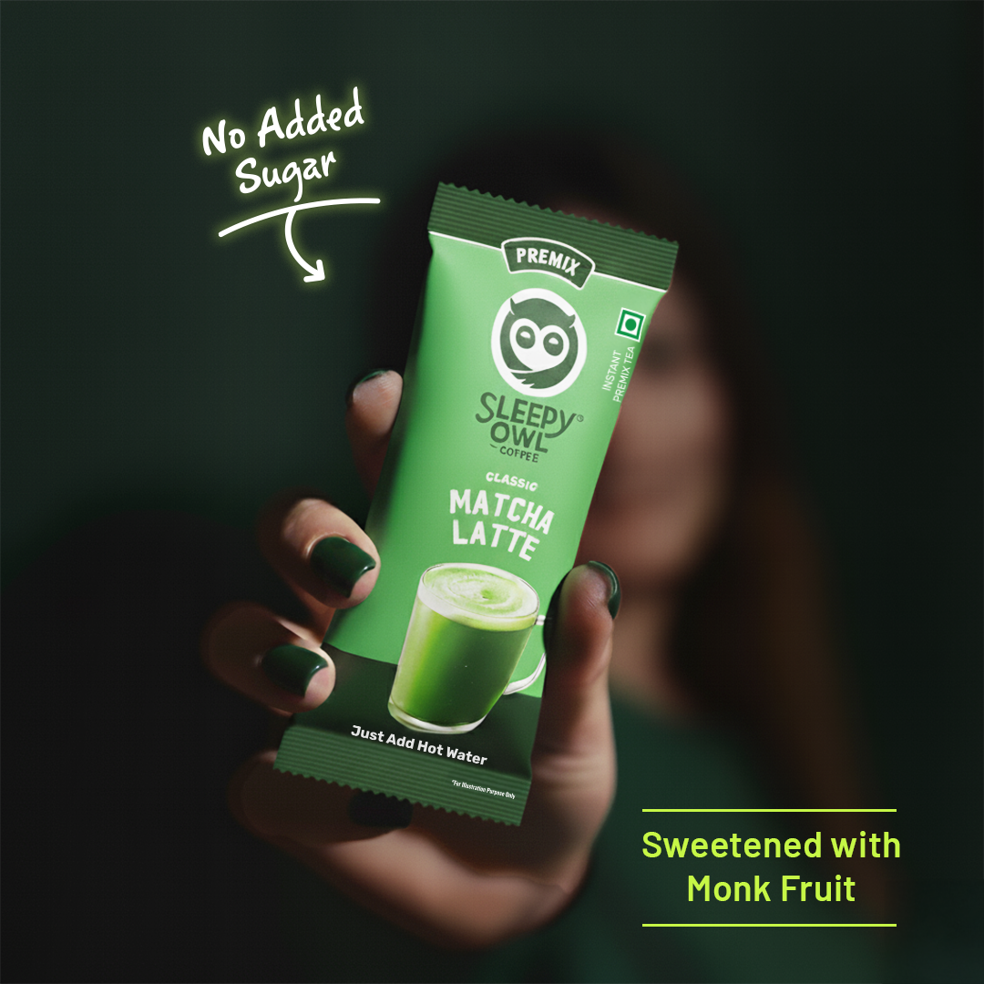 Hand holding a Sleepy Owl Matcha Latte packet, labeled 'No Added Sugar' and 'Sweetened with Monk Fruit.'
