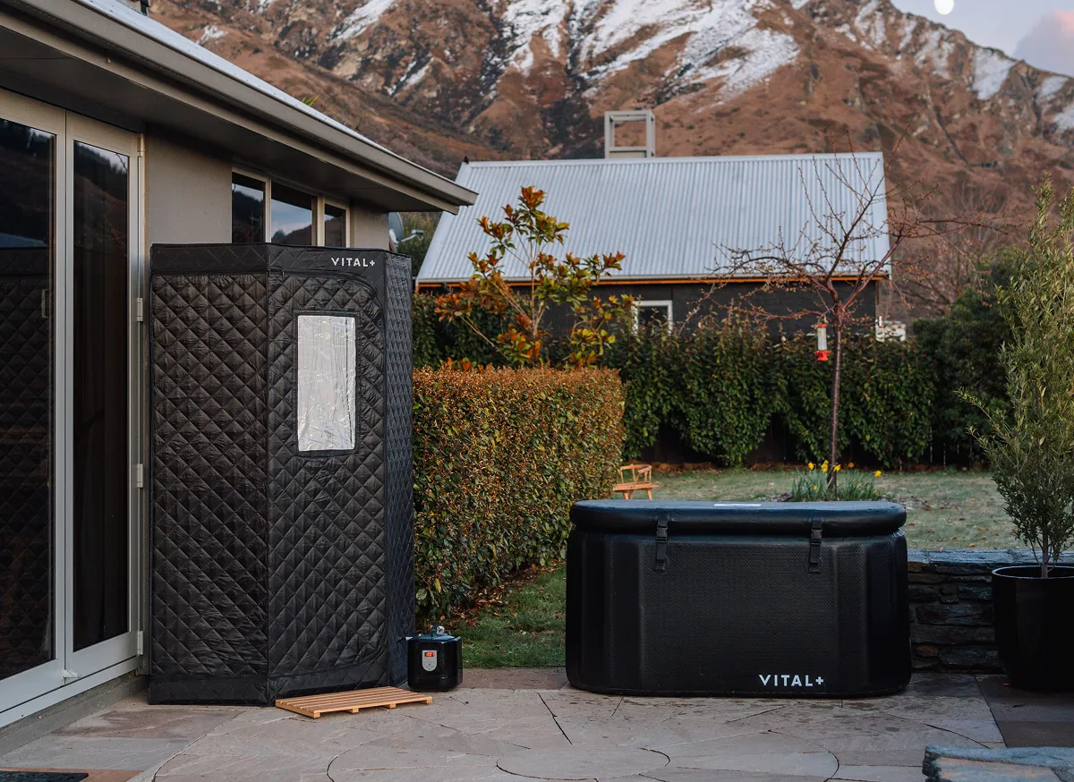A portable sauna and ice bath sit on a patio with a snowy mountain in the background.