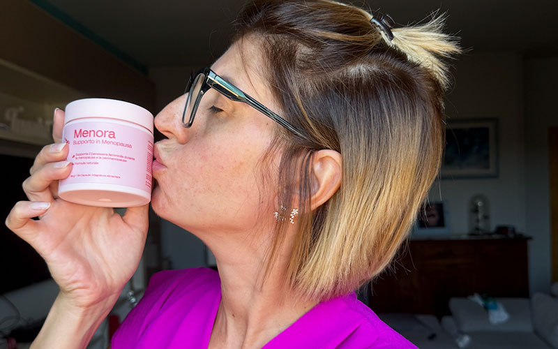 Smiling person holding a pink jar of skincare cream, with red flowers in the background.