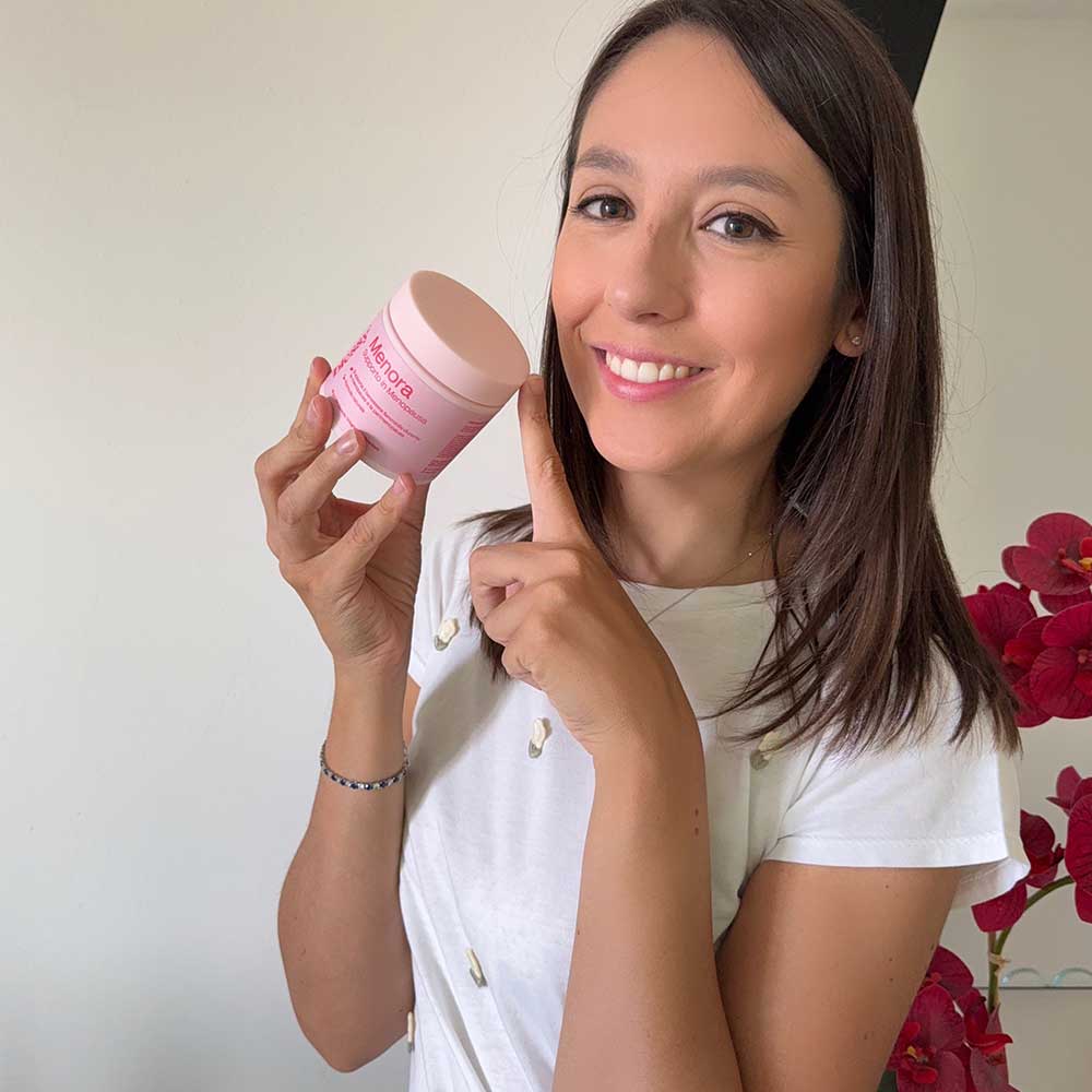Smiling person holding a pink jar of skincare cream, with red flowers in the background.