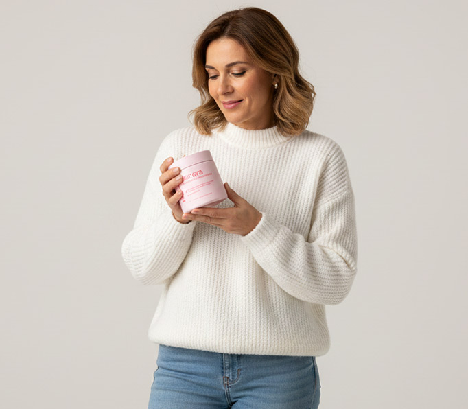 Donna con un contenitore rosa, che indossa un maglione bianco e jeans.