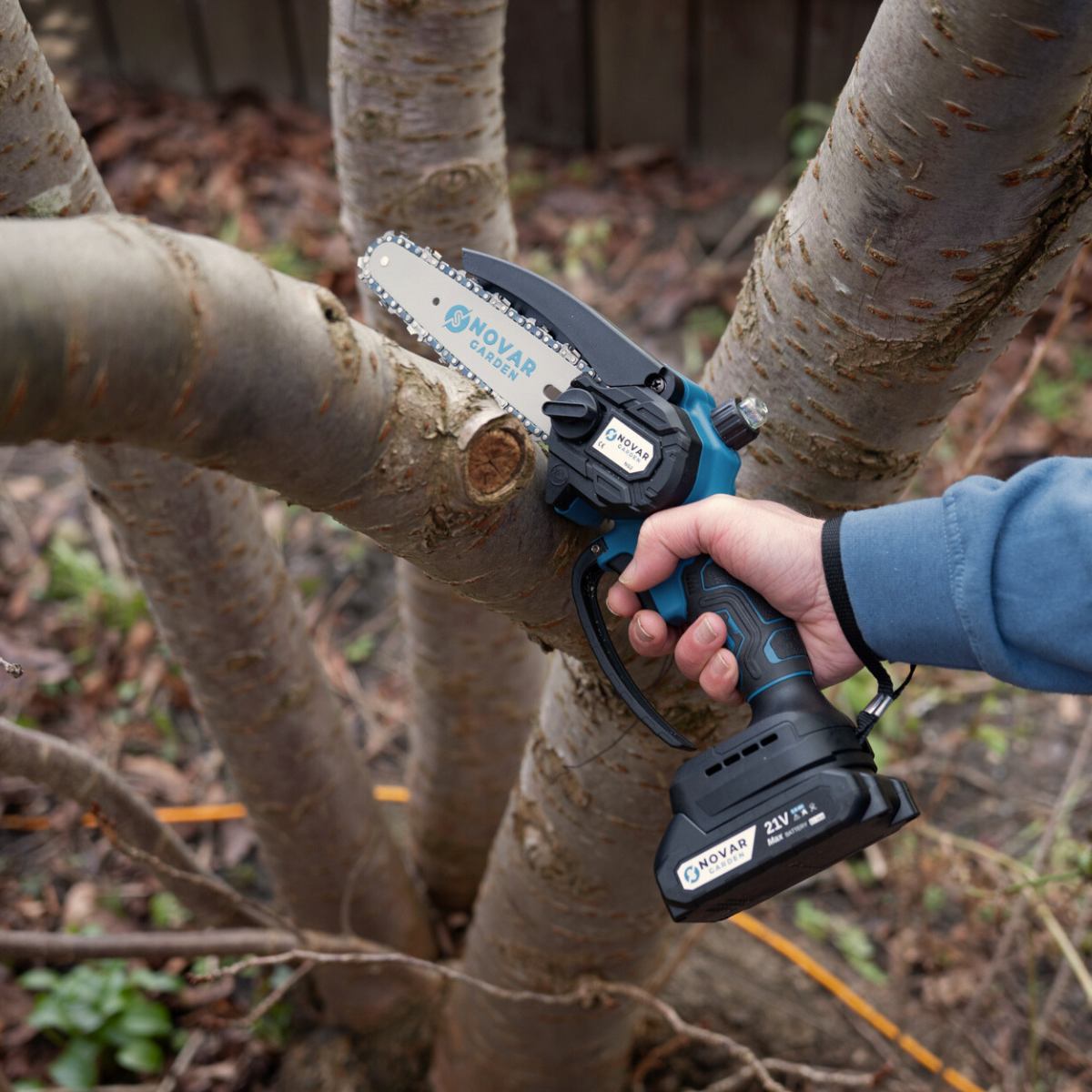 Person using a handheld electric chainsaw to cut a tree branch.