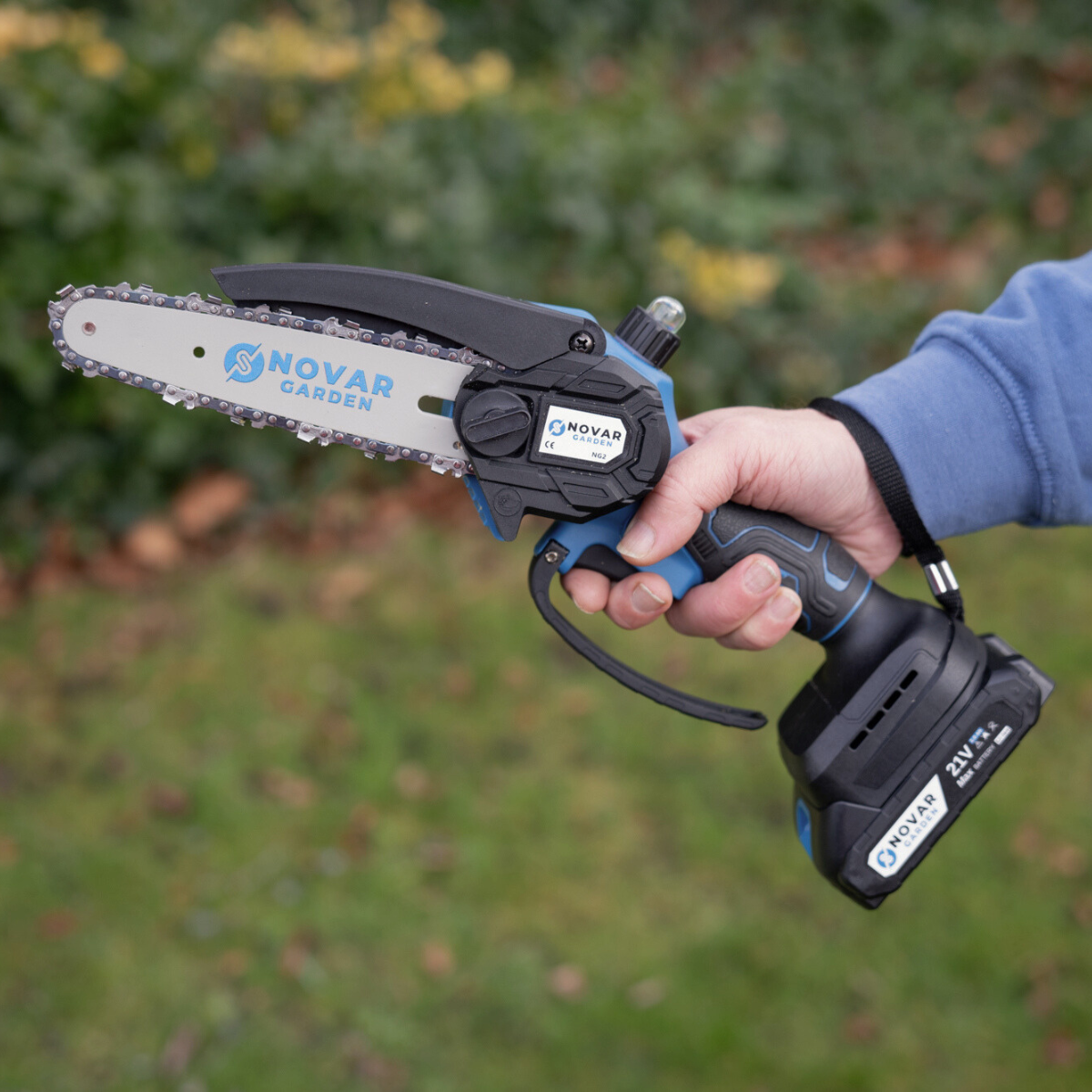 A hand holding a Novar Garden cordless mini chainsaw outdoors.
