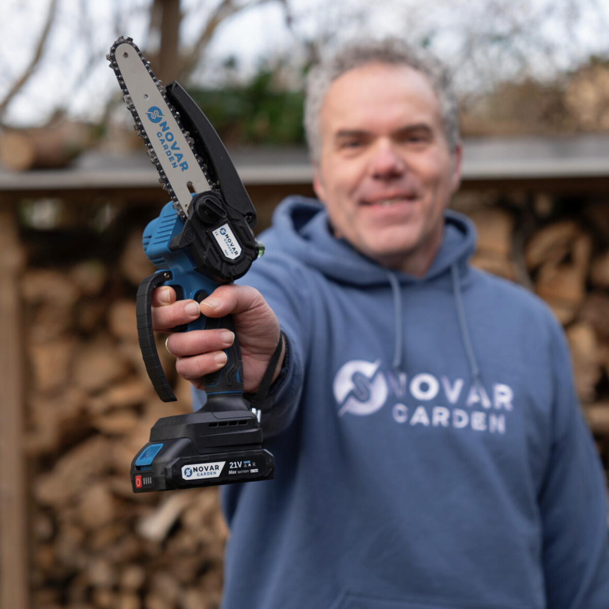 Person holding a small chainsaw in front of a woodpile.