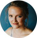 Person with light hair smiling against a blue background.