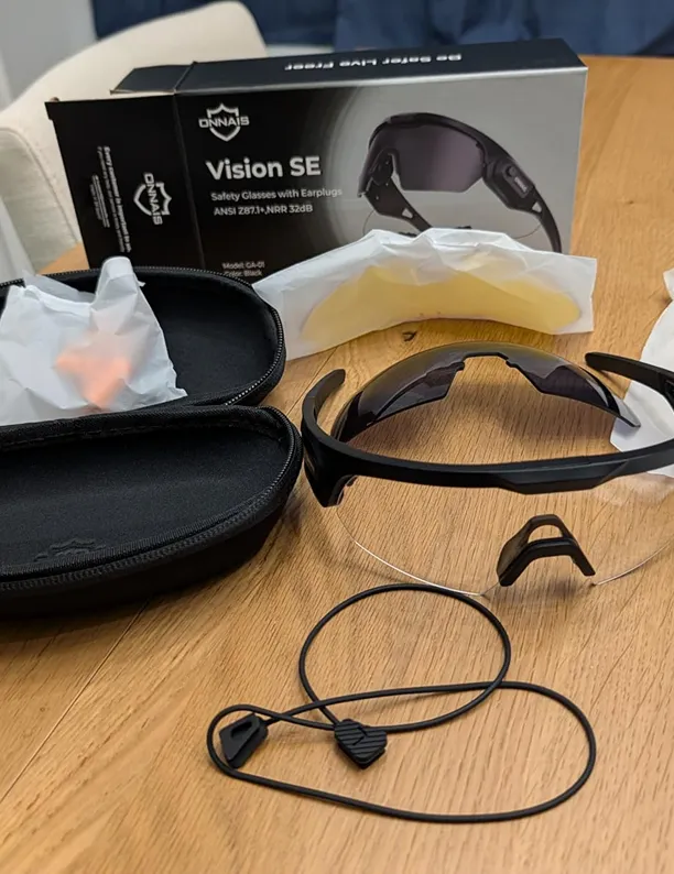 A set of safety glasses with their box, case, and accessories laid out on a wooden table.