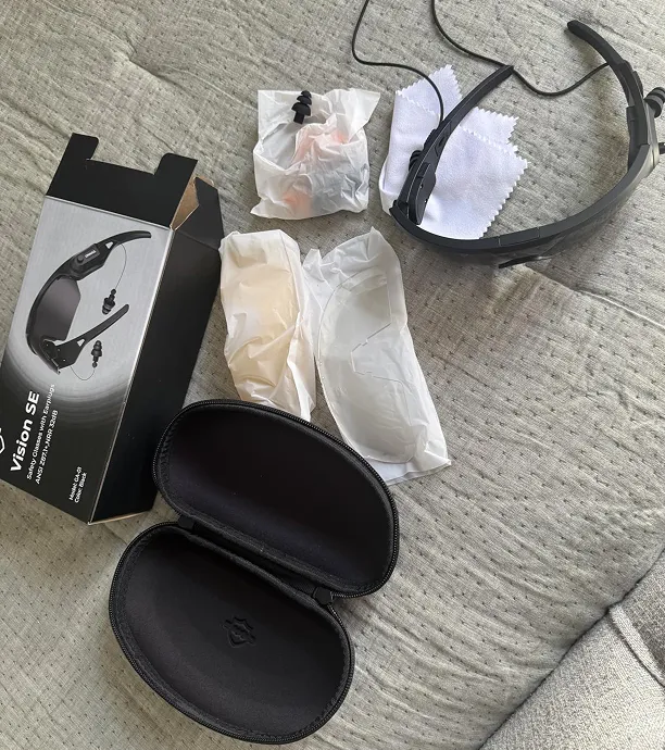 Vision SE safety glasses with earplugs unboxed with the case, packaging, and accessories on a gray surface.
