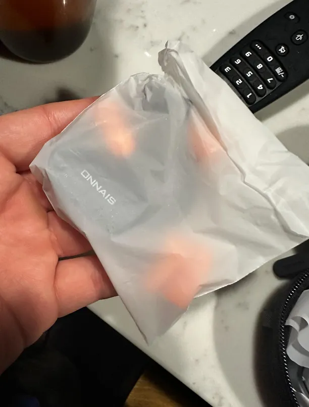 A hand holds a small gray electronic device from the brand ONNAIS, wrapped in translucent plastic.