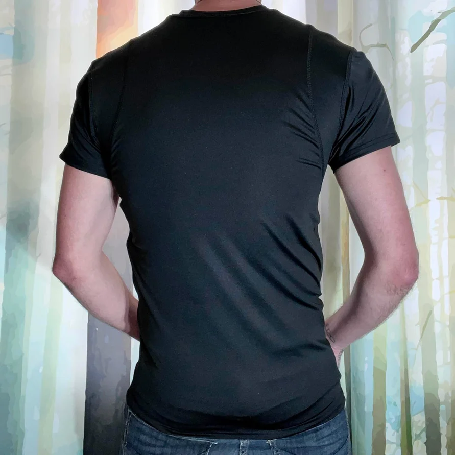 The back of a man wearing a black t-shirt and jeans, with his arms behind his back.