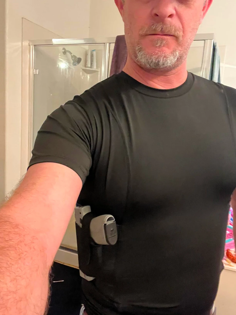 A man wearing a black compression shirt with a handgun in an underarm holster.