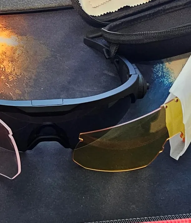 A pair of black sunglasses with interchangeable lenses in yellow and pink, next to a black case.