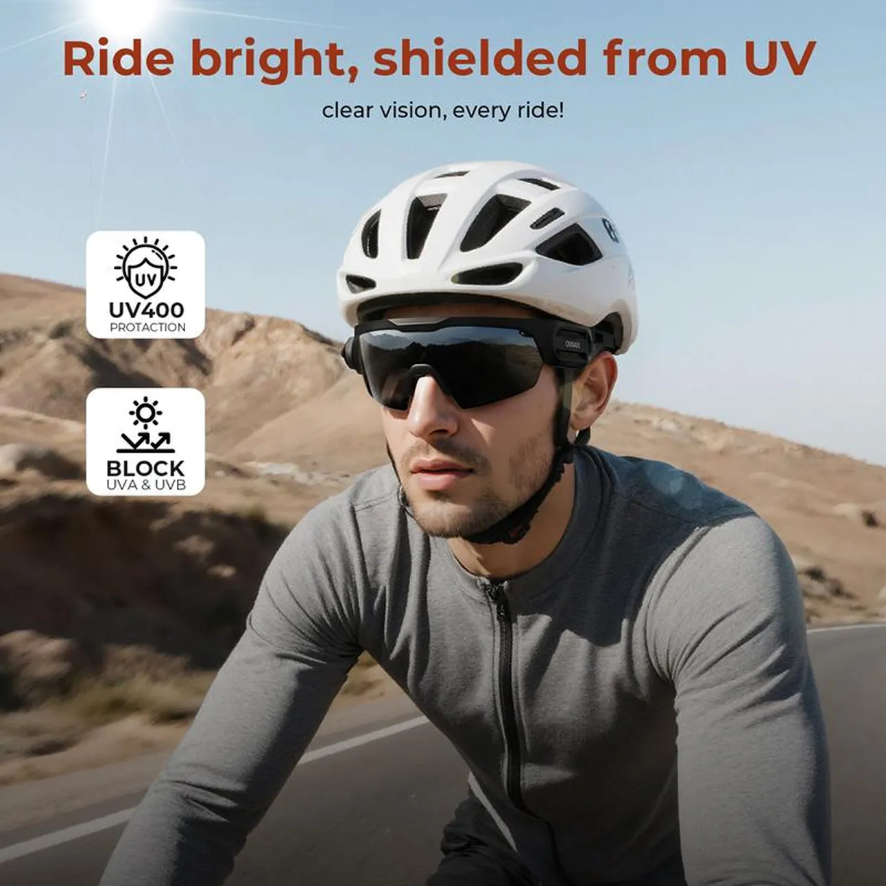 A man wearing a bicycle helmet and sunglasses rides on a road through a sunny, dry landscape.