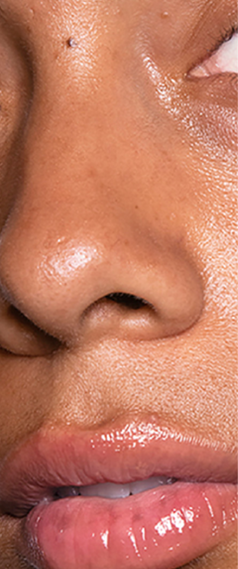 An extreme close-up of a person's face showing their nose and glossy lips with dewy skin.