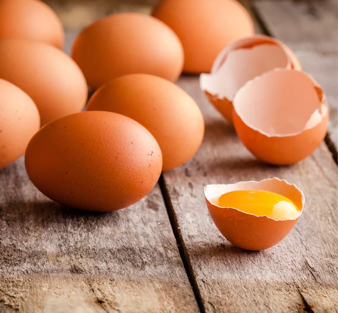 A close-up of several brown eggs on a rustic wooden surface, with one cracked open.