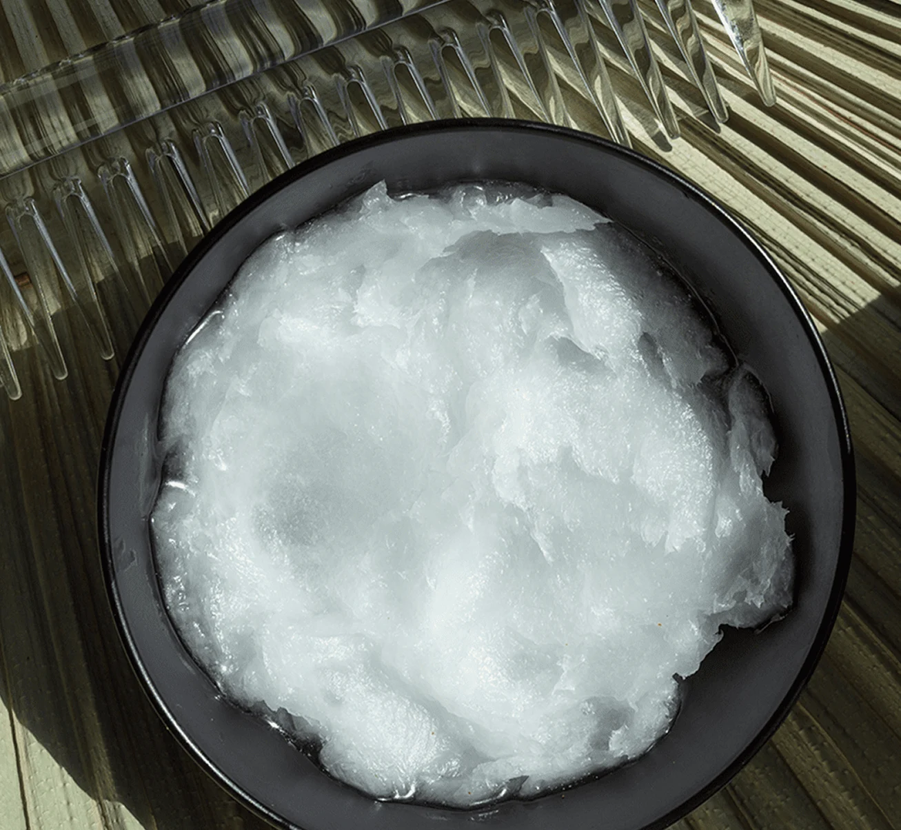 An overhead shot of a dark bowl with a white, solid substance next to a clear comb.