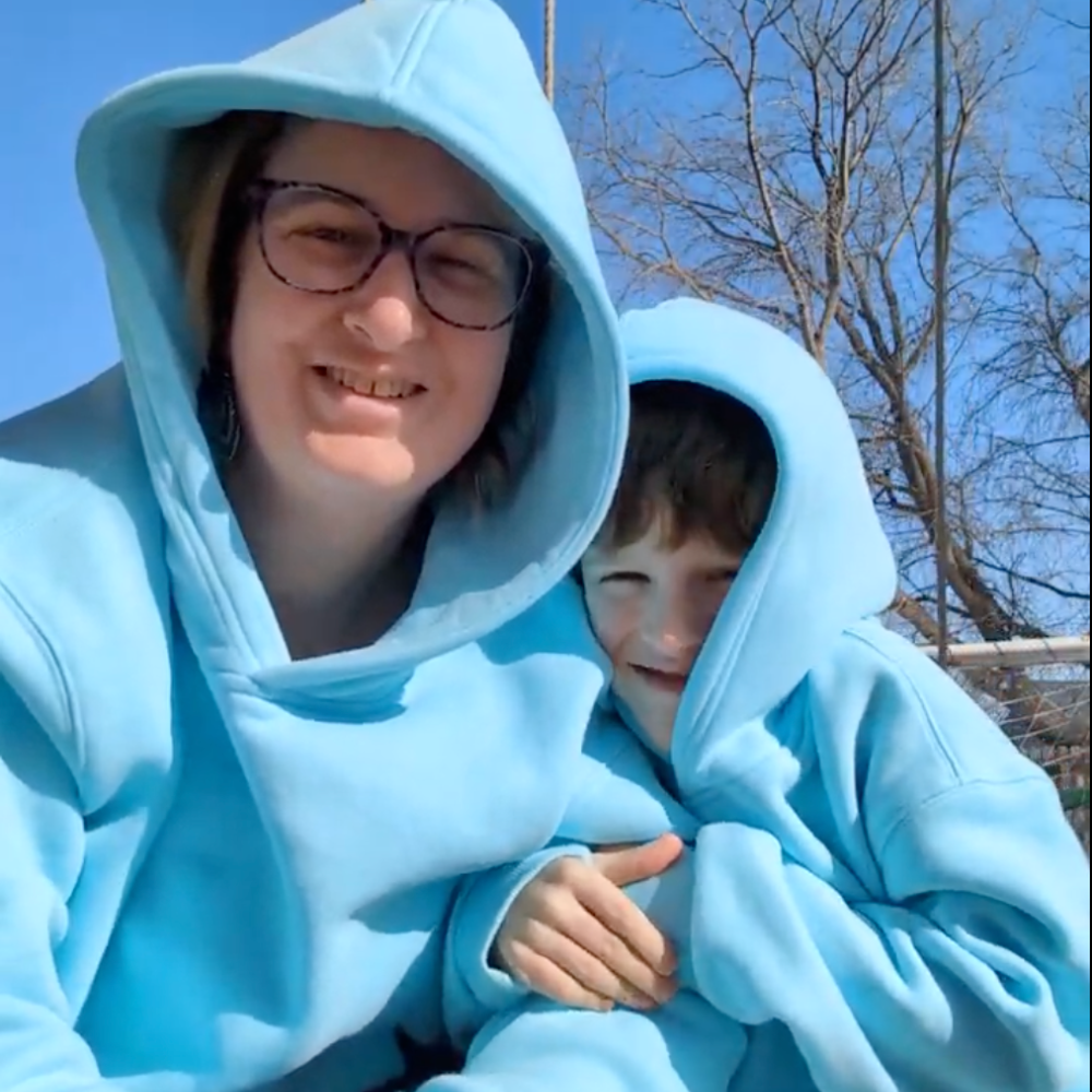 Two people in blue hoodies smiling outdoors on a sunny day.