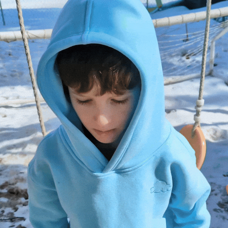 Child in blue hoodie standing near a swing in snowy playground.