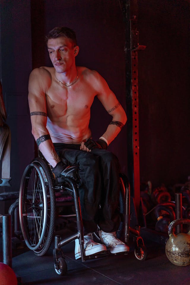 Man in wheelchair wearing athletic clothing, sitting in a gym setting.