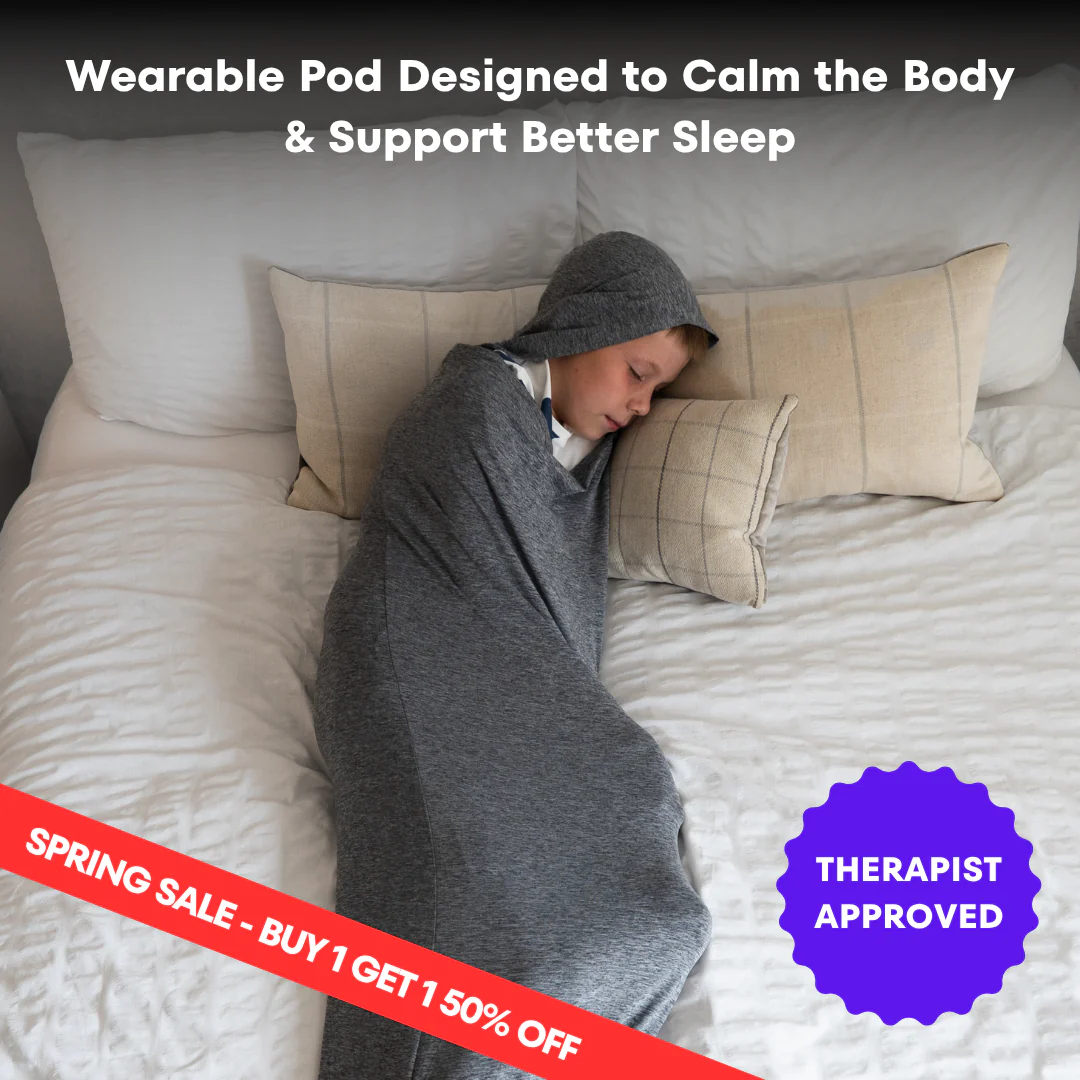 A child sleeps in a bed while enclosed in a grey, hooded wearable blanket.