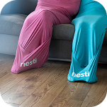 Two people in pink and turquoise full-body stretch sacks are on a couch and the floor.