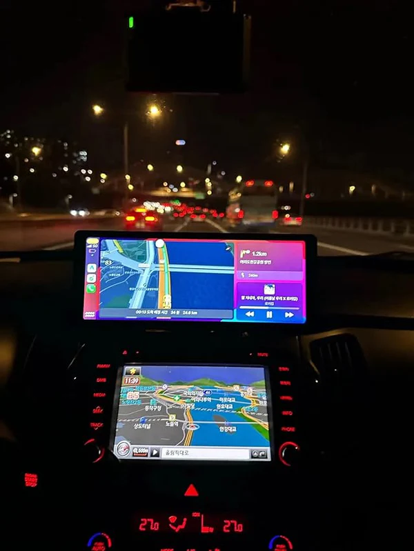 Car dashboard at night with two GPS screens and city lights outside.